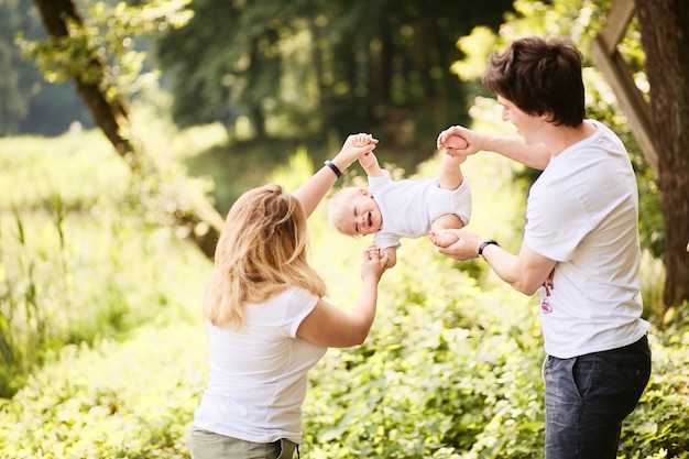 Bezpłatne zdjęcie szczęśliwa rodzina. mama i tata bawią się z małym synkiem odpoczywającym w zielonym letnim parku