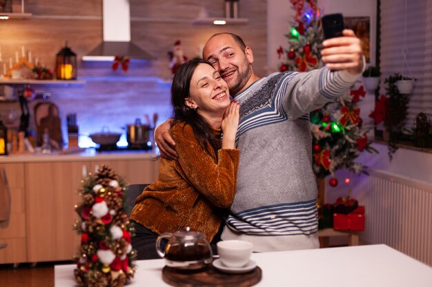 Szczęśliwa rodzina uśmiechnięta podczas robienia selfie przy użyciu nowoczesnego smartfona