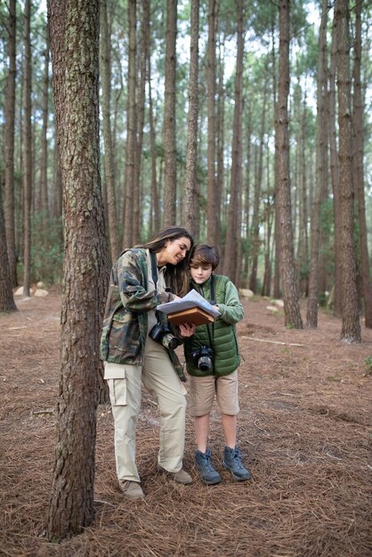 Szczęśliwa rodzina z kamerami spaceru w lesie. Ciemnowłosa mama i syn w płaszczach szykują się do robienia zdjęć, omawiają trasę. Koncepcja rodzicielstwa, rodziny, wypoczynku