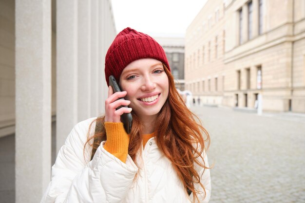 Bezpłatne zdjęcie szczęśliwa rudowłosa dziewczyna z rozmowami telefonicznymi rozmawia przez aplikację mobilną za pomocą internetu, aby dzwonić za granicę