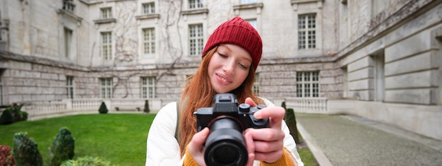 Bezpłatne zdjęcie szczęśliwa rudowłosa turystka robi zdjęcia fotografowi z profesjonalnym aparatem i spaceruje po mieście