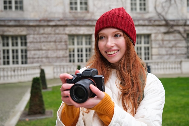 Szczęśliwa rudowłosa turystka robi zdjęcia fotografowi z profesjonalnym aparatem spacerującym po mieście i