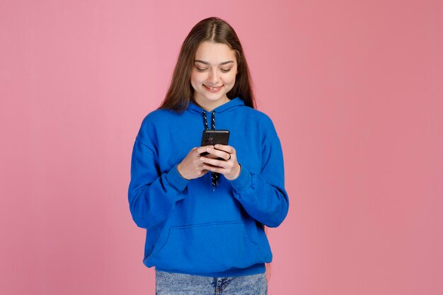 Szczęśliwa skoncentrowana kobieta w bluzie i dżinsach wysyła wiadomości na telefon komórkowy, patrząc na ekran
