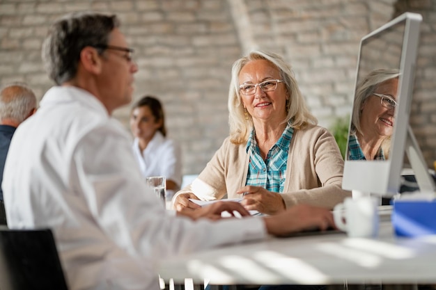 Bezpłatne zdjęcie szczęśliwa starsza kobieta komunikująca się z lekarzem podczas analizowania danych medycznych na komputerze w klinice