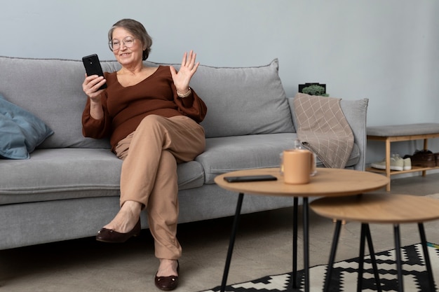Bezpłatne zdjęcie szczęśliwa starsza kobieta korzystająca ze smartfona w salonie nowoczesnego mieszkania