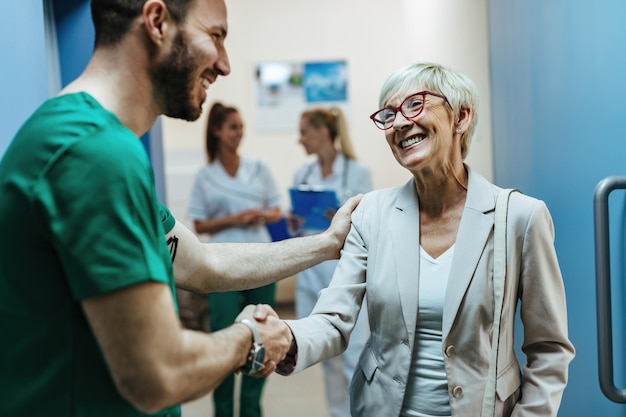 Szczęśliwa starsza kobieta ściska dłoń chirurgowi na korytarzu szpitala