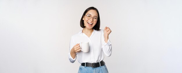 Szczęśliwa tańcząca kobieta pijąca kawę lub herbatę z kubka koreańskiej dziewczyny z kubkiem stojącym na białym tle