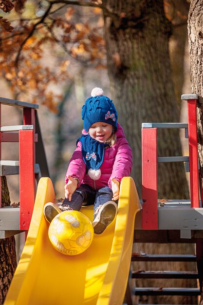 Szczęśliwa trzyletnia dziewczynka w kurtce na slajdzie w parku