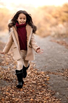 Szczęśliwa urocza dziewczynka biega w jesiennym parku. szczęśliwe dzieciństwo