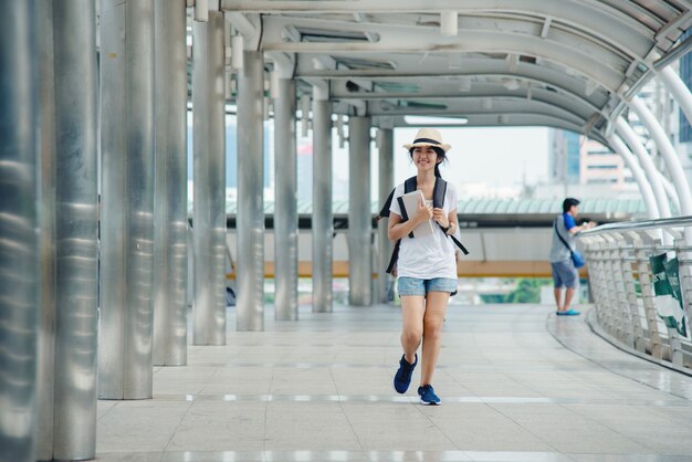 Szczęśliwa uśmiechnięta Azjatycka studencka dziewczyna z plecakiem przy miasta tłem