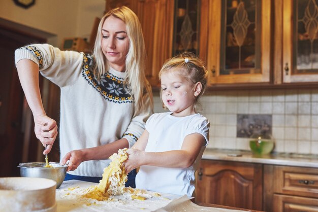 Szczęśliwa uśmiechnięta mama w kuchni piec ciastka z jej córką.