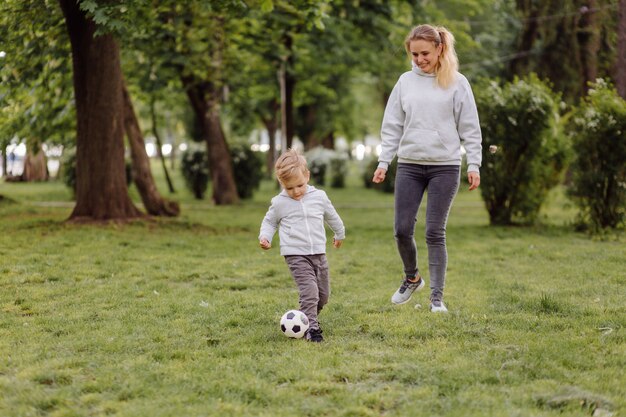 Szczęśliwa uśmiechnięta matka i synowie bawić się z futbolową piłką outdoors