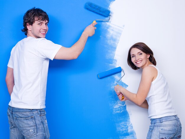 Szczęśliwa wesoła młoda para szczotkuje ścianę w kolorze niebieskim