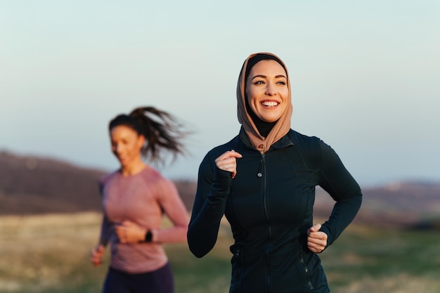 Szczęśliwa wysportowana kobieta ciesząca się porannym biegiem z instruktorem fitness w przyrodzie