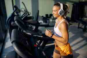 Bezpłatne zdjęcie szczęśliwa wysportowana kobieta ze słuchawkami biegająca na bieżni w siłowni