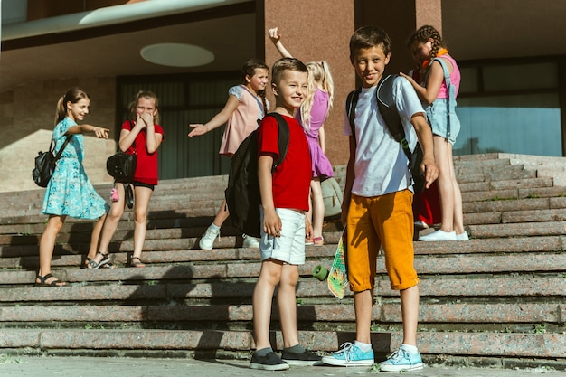 Szczęśliwe dzieci bawiące się na ulicy miasta w słoneczny letni dzień przed nowoczesnym budynkiem. Grupa szczęśliwych dzieci lub nastolatków, wspólna zabawa. Pojęcie przyjaźni, dzieciństwa, lata, wakacji.