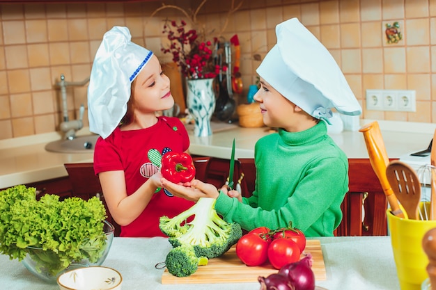 Szczęśliwe dzieci przygotowują sałatki ze świeżych warzyw w kuchni