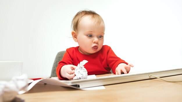 Szczęśliwe dziecko dziewczynka siedzi z klawiaturą nowoczesnego komputera lub laptopa na białym tle na białym studio.