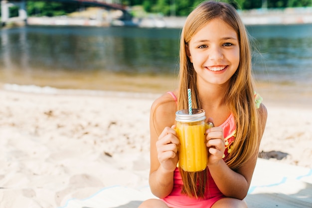Bezpłatne zdjęcie szczęśliwe dziecko uśmiecha się z napojem na plaży