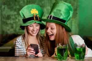 Bezpłatne zdjęcie szczęśliwe koleżanki świętują ul. patrick's day razem w barze ze smartfonem
