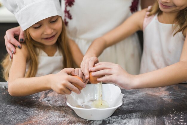 Szczęśliwe małe dziewczynki łamania jajka w pucharze nad kuchennym worktop