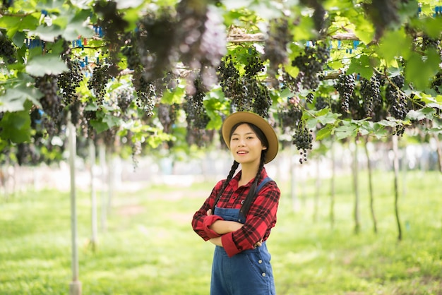 Bezpłatne zdjęcie szczęśliwe młode kobiety ogrodniczki mienia gałąź dojrzały błękitny winogrono