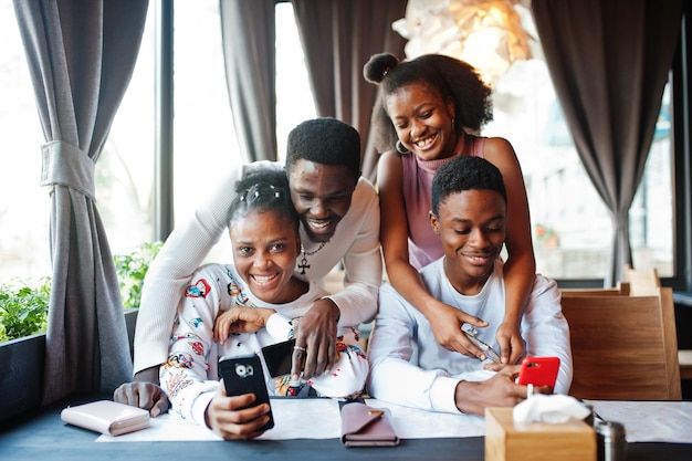 Bezpłatne zdjęcie szczęśliwi afrykańscy przyjaciele siedzący i rozmawiający w kawiarni grupa czarnych ludzi spotykających się w restauracji przytula się i patrzy na swój telefon komórkowy