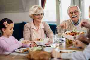 Bezpłatne zdjęcie szczęśliwi dziadkowie jedzą obiad z rodziną przy stole jadalnym