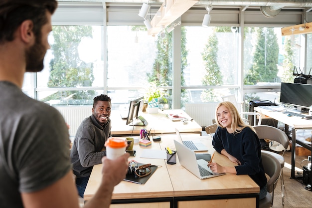 Bezpłatne zdjęcie szczęśliwi młodzi koledzy siedzi w biurowym coworking