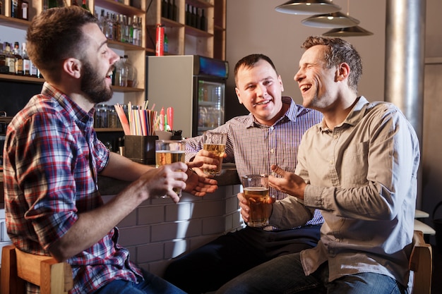 Szczęśliwi przyjaciele pije piwo przy kontuarem w pubie