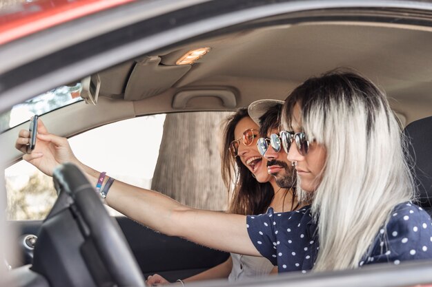 Szczęśliwi przyjaciele siedzi wśrodku samochodowego bierze selfie przez telefonu komórkowego