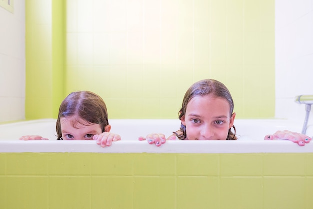 Szczęśliwi roześmiani siostra dzieciaki kąpać się bawić się z piankowymi bąblami. małe dzieci w wannie. rodzinny styl życia w pomieszczeniu