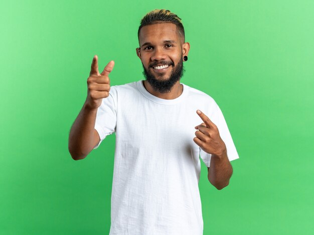 Szczęśliwy afroamerykanin młody człowiek w białej koszulce patrzący na kamerę uśmiechający się radośnie wskazujący palcem wskazującym na kamerę