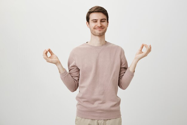 Szczęśliwy atrakcyjny facet medytuje, trzymaj ręce na boki z gestem zen