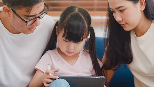 Szczęśliwy azjatycki rodzinny tata, mama i córka, siedząc na sofie w salonie w domu za pomocą technologii tabletu komputerowego