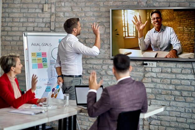 Szczęśliwy biznesmen prowadzący wideokonferencję i powitanie ze swoim zespołem, który pracuje w biurze