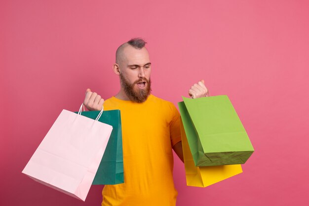 Szczęśliwy brodaty pozytywny mężczyzna dorywczo wygląd z kolorowe torby na zakupy studio różowym tle