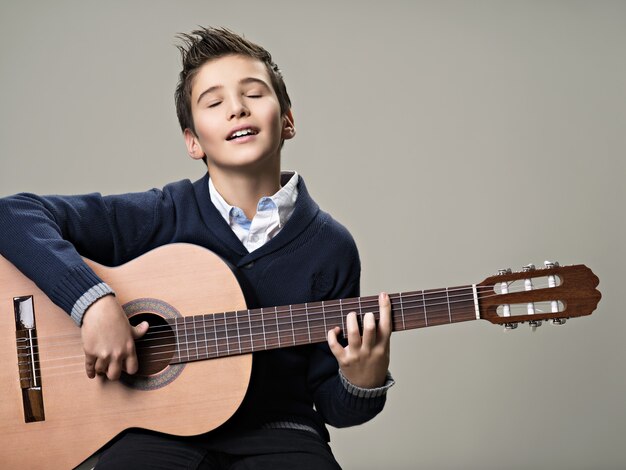 Szczęśliwy chłopiec gra z przyjemnością na gitarze akustycznej.