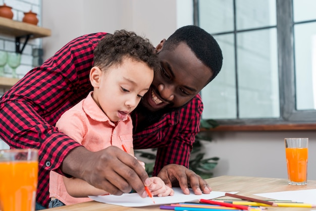 Szczęśliwy czarny ojciec i syn rysuje przy stołem