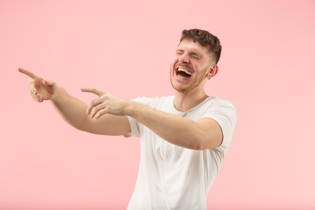 Szczęśliwy człowiek biznesu stojąc i uśmiechając się na białym tle na różowym tle studio. Piękny portret męski w połowie długości. Młody człowiek emocjonalny.