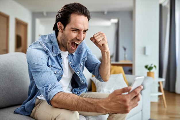 Szczęśliwy człowiek czyta dobre wieści przez smartfona i świętuje w domu