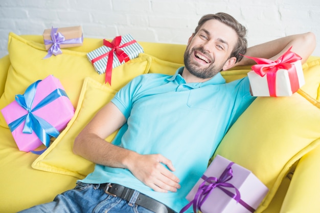 Szczęśliwy człowiek pochylony na kanapie z różnych prezentów urodzinowych