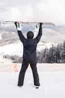 Bezpłatne zdjęcie szczęśliwy człowiek stojący z snowboard nad głową na szczycie wzgórza gór