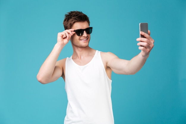 Szczęśliwy człowiek w okularach przeciwsłonecznych zrobić selfie przez telefon