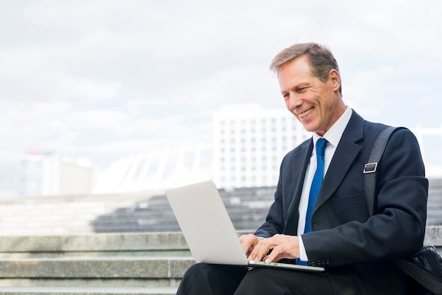 Szczęśliwy dojrzały biznesmen pracuje na laptopie przy outdoors