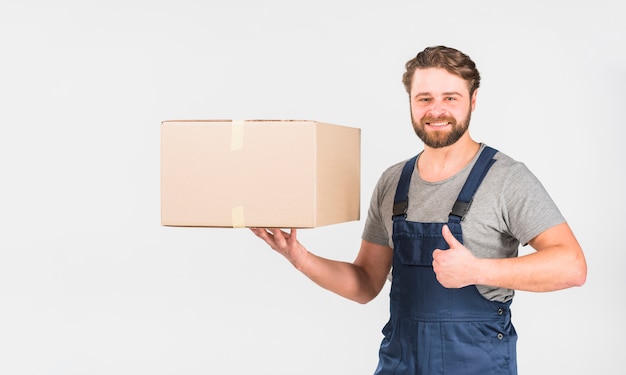 Bezpłatne zdjęcie szczęśliwy doręczeniowy mężczyzna z pudełkowatym pokazuje kciukiem up