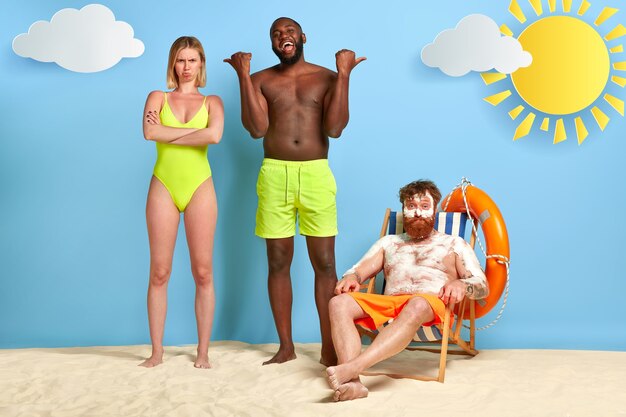 Szczęśliwy facet wskazuje na rudą pozę z filtrem przeciwsłonecznym na plaży
