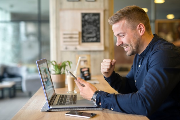 Szczęśliwy freelancer z tabletem i laptopem w kawiarni