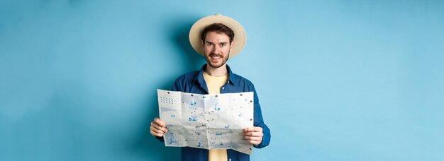 Bezpłatne zdjęcie szczęśliwy i pozytywny facet na wakacjach patrzący w kamerę i trzymający uśmiechniętą mapę podekscytowany latem