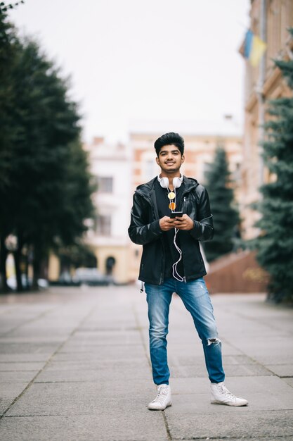 Szczęśliwy indyjski mężczyzna chodzi mądrze telefon i używa słuchać słuchawki z muzyką